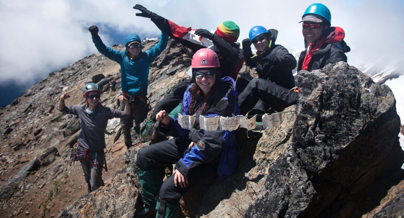 a group of outward bound students wearing safety gear appear to celebrate at the top of the mountain